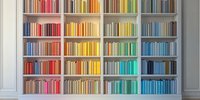 Colorful books arranged by spectrum colors on white wooden built-in shelves create rainbow pattern. Modern minimalist library interior design for home office.