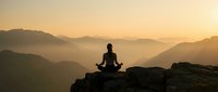 Person meditating on mountain peak at sunrise with layered mountain ranges in misty golden light creating peaceful zen atmosphere for wellness content.