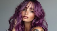 Young Caucasian woman with vibrant purple wavy hair, freckles, and shoulder tattoo against neutral gray background for beauty and hair color advertising.