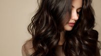 Young woman with luxurious wavy brunette hair against neutral beige background, showcasing healthy shiny locks for hair care advertising.