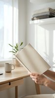 Person holding rolled beige fabric in bright minimalist workspace with wooden desk, potted plant, white shelving, and natural window light for home organization and interior design concepts.