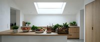 Modern minimalist kitchen interior with wooden countertops, fresh vegetables, natural skylight illumination, clean white walls and contemporary cabinetry design.