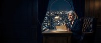 Senior businesswoman with gray hair working at wooden desk with laptop in dark office overlooking illuminated cityscape at night, professional environment for corporate business concepts.