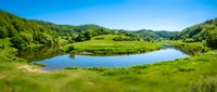 Scenic river bend winding through lush green valley with forested hills under clear blue sky, suitable for travel, nature, and environmental design projects.