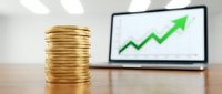 Stacked gold coins with upward trending graph on laptop screen, representing financial growth, investment success, and rising profits.