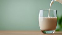 Fresh milk pouring into clear glass on wooden table against mint green background, creating dynamic splash and flow effect. Suitable for food and beverage advertising.