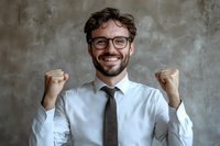 Excited Caucasian businessman in glasses and tie celebrating success with raised fists against textured gray wall background, showing positive emotion and victory.