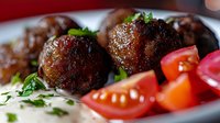 Delicious homemade meatballs with fresh herbs and tomato slices on white plate. Traditional comfort food for family dinner and restaurant menu.