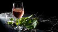 Elegant rosé wine glass with fresh mint leaves on dark marble surface for sophisticated dining and beverage photography.