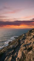 Dramatic coastal cliffs meet golden sunset sky with vibrant orange and pink hues reflecting over calm ocean waters, ideal for travel and nature backgrounds.