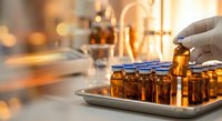 Laboratory scientist in protective gloves handling amber glass vials in modern research facility with warm lighting for pharmaceutical development.