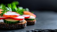 Fresh vegetable sandwiches on dark rye bread with radish, cucumber slices and herbs against black stone background, macro food photography.