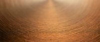 Copper metal surface with circular brushed texture and warm golden reflections creating radial pattern for industrial and manufacturing backgrounds.
