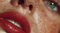 Close-up portrait of young Caucasian woman with freckled skin, red glossy lipstick and green eyes. Natural beauty and skincare concept for cosmetics.