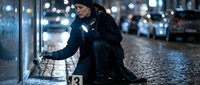 Young homeless woman sitting on wet city street at night with cardboard sign asking for help during winter cold weather with urban lights background.