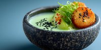 Creamy green soup with sesame seeds and crispy garnish served in rustic stone bowl, gourmet restaurant presentation for culinary arts and fine dining.