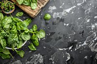 Fresh green spinach leaves on dark stone background with water drops and rustic wooden cutting board, raw organic produce for healthy cooking.