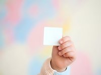 Caucasian hand holding blank white card against soft pastel gradient background with pink, blue, and yellow tones. Use for business cards, gift cards, vouchers, or promotional materials.