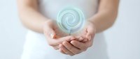 Woman in white holding glowing green energy spiral above cupped hands representing healing power, wellness therapy, and spiritual energy work.