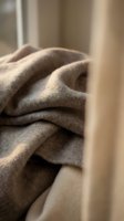 Folded beige and gray wool blanket or throw fabric with soft texture and natural folds, suitable for home decor, lifestyle, and textile design projects.