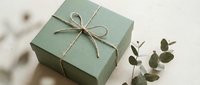 Sage green gift box tied with natural twine bow alongside eucalyptus branch on neutral background for eco-friendly packaging and sustainable gifting concepts.