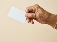 Senior man with medium skin tone holding blank white card against neutral beige background, suitable for business card mockups, identity design, and corporate branding projects.
