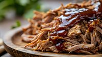 Tender shredded pulled pork with rich barbecue sauce served on rustic wooden plate, slow-cooked meat for sandwiches and comfort food meals.