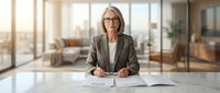Professional mature Caucasian businesswoman with glasses sitting at conference table in modern office, reviewing documents during meeting preparation.