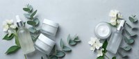 Natural skincare cosmetic products with eucalyptus leaves and white flowers on marble background for beauty and wellness routine.