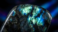 Polished labradorite gemstone displaying brilliant blue and green iridescent flashes against dark matrix on cosmic background for jewelry and mineral collection.