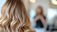 Blonde wavy hair close-up with soft bokeh background in beauty salon. Professional hairstyling and coloring result showing natural balayage technique.