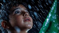 Young Asian woman with wet face and dramatic expression in rain shower, water droplets falling, artistic beauty portrait with green accent lighting and dark background.