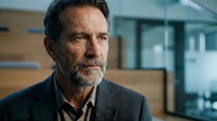 Middle-aged Caucasian man with salt-and-pepper beard wearing gray blazer and dark shirt in modern office setting, suitable for corporate, business, and professional themes.