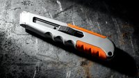 Professional utility knife with orange and black handle on weathered concrete surface for construction and crafts projects.