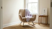 Cozy modern armchair with lavender throw blanket in bright minimalist room with wooden side table and window light.
