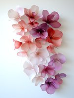 Delicate paper flowers in shades of pink, coral and purple cascade on white background. Handcrafted floral art arrangement creates soft romantic composition.
