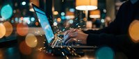 Professional businessman working late on laptop computer in modern office with warm bokeh lights creating atmospheric evening workspace ambiance for productivity concepts.