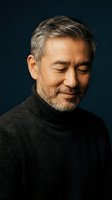 Mature Asian man with gray beard smiling peacefully in dark turtleneck sweater against navy background for lifestyle and wellness content.
