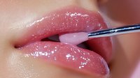 Macro shot of glossy pink lips during professional makeup application with fine detail brush showing cosmetic application technique and lip gloss texture.