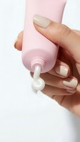 Hand holding pink cosmetic tube with cream product dispensed, showcasing skincare, beauty, cosmetics, and personal care applications for packaging design.