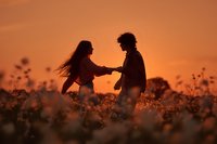 Romantic couple silhouettes holding hands in flower field during golden sunset creating intimate moment for wedding and love concepts.