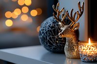 Festive winter decoration with golden reindeer figurine, ornate glass bauble, and glowing candle against blurred bokeh lights creating cozy holiday atmosphere.