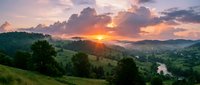 Dramatic sunset over rolling green hills and distant mountains with a winding river, ideal for travel, nature, and landscape design projects.