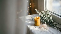 Cozy bathroom scene with burning candle and eucalyptus branches on bathtub edge creating spa-like atmosphere for relaxation and self-care rituals.
