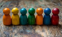 Colorful wooden pawn figures arranged in rainbow order on rustic wood background, representing diversity, unity and teamwork in business or education.