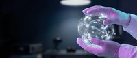 Scientist hands in purple gloves holding transparent glass brain model in modern laboratory for medical research and neuroscience education.