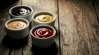 Four colorful gourmet sauces in ceramic bowls on rustic wooden table for culinary cooking and food preparation.