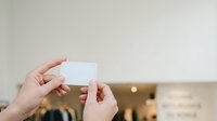 Hands holding blank white card or business card mockup with blurred interior background for branding and marketing purposes.