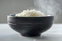 Steaming hot white rice served in traditional black ceramic bowl on light surface, perfect for food photography and culinary presentations. Minimalist Asian cuisine concept.