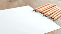 Sharpened wooden pencils arranged in diagonal line next to blank white paper on rustic wooden desk surface, minimalist composition for creative workspace.